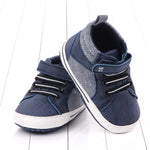 Pair of blue children's shoes with white soles on a light wooden floor.