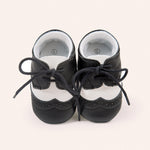 Pair of black and white baby shoes with laces on a light beige background