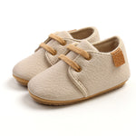 Pair of beige baby shoes with brown laces on a white background