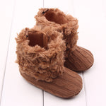 Pair of brown knitted boots with fluffy texture on a white wooden surface