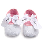 Pink and white baby shoes with 'Angel' bow on a white background