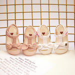 Set of four pairs of pink children's sandals with heart designs on a textured surface.