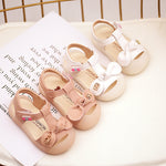 Pair of pink children's sandals with bows on a white surface.