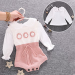 Baby outfit with white long-sleeve top and pink knitted shorts on a gray background.