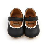 Pair of black baby shoes with brown soles on a white background