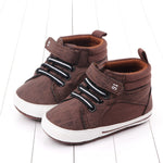 Pair of brown children's shoes with white soles on a light wooden floor.