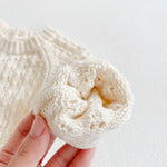 Hand holding a white knitted item against a light background