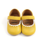 Pair of yellow baby shoes with white scalloped edges on a white background