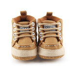 Pair of tan baby shoes with white laces on a white background