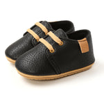 Pair of black leather shoes with tan laces and sole on a white background