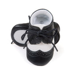 Black leather baby shoes with white soles on a white background