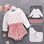 Baby outfit with white top and pink polka dot shorts on a gray background