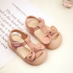 Pair of pink children's sandals with bows on a light background