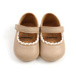 Pair of beige baby shoes with scalloped edges on a white background
