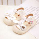 Pair of white baby sandals with decorative straps on a light background