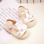 Pair of white children's sandals with bows on a newspaper background