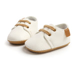 White baby shoes with brown soles and laces on a white background