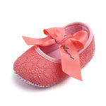 Pink baby shoes with a large bow on a white background