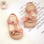 Pair of pink baby sandals with bow details on a white surface with text.