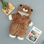 Brown bear-themed baby onesie on a gray background with a magazine and flowers.